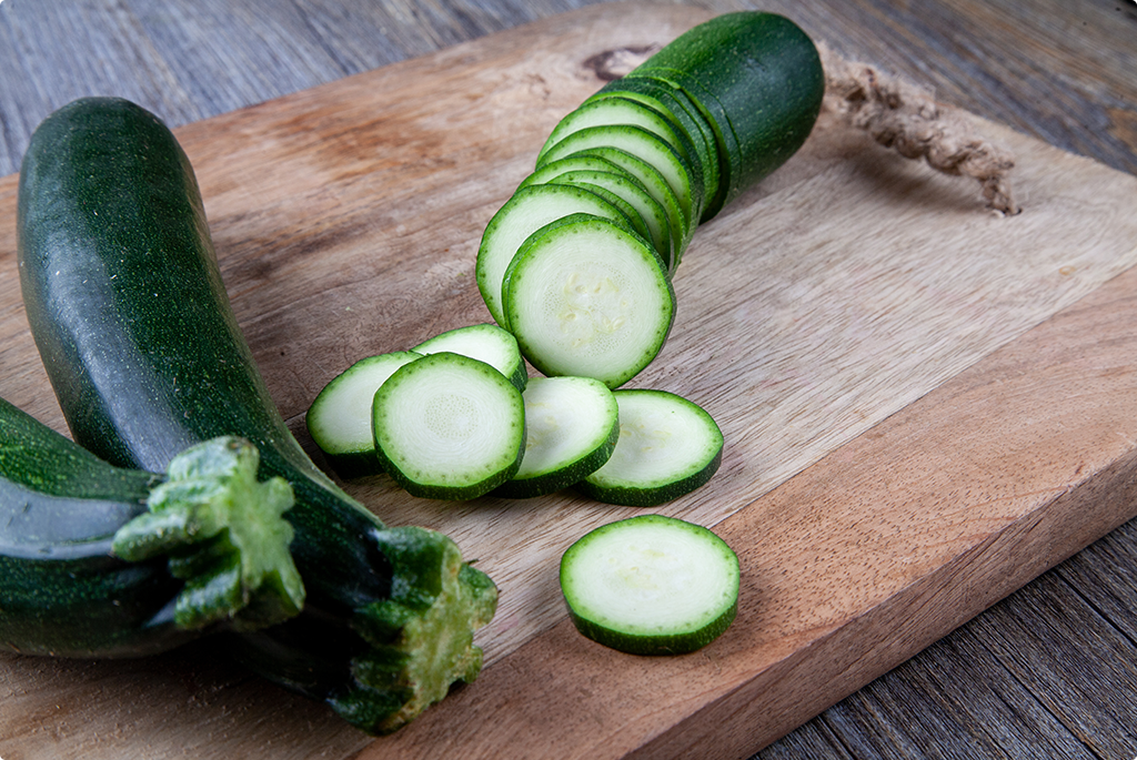 Courgettes on wooden chopping board with one sliced into circles